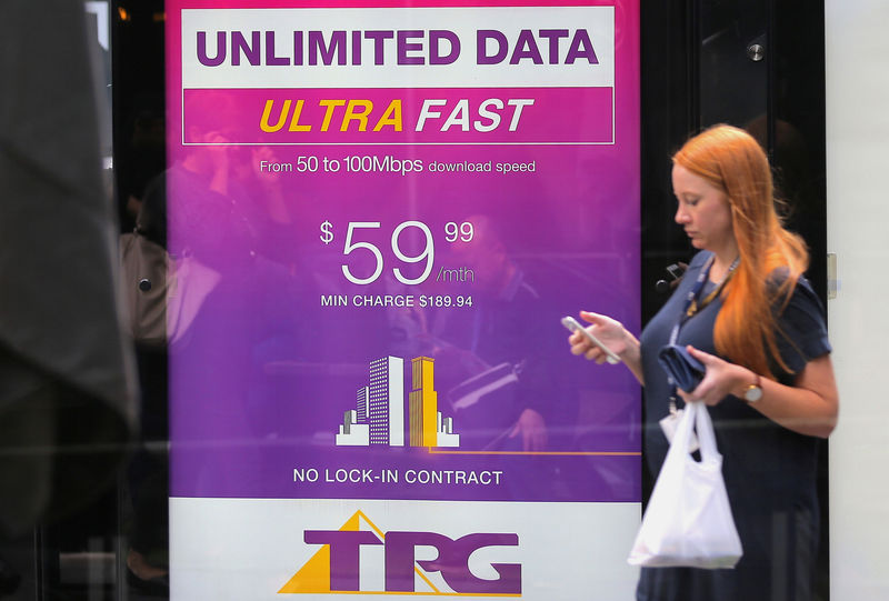 © Reuters. A woman looks at her phone as she walks past an advertisement for Australia's TPG Telecom Ltd in central Sydney, Australia