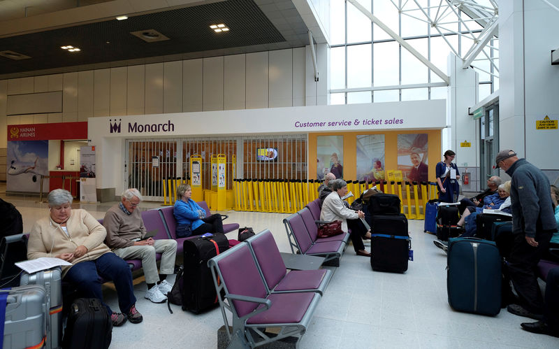 © Reuters. FILE PHOTO: Passengers sit outside a Monarch airlines customer service office after the airline ceased trading, at Manchester airport