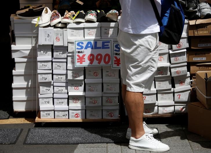 © Reuters. A shopper looks at shoes next to signs advertising sales at a shopping district in Tokyo