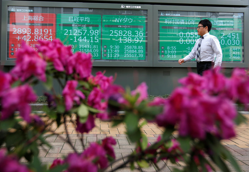 © Reuters. FILE PHOTO: A passerby walks past in front of a stock quotation board outside a brokerage in Tokyo