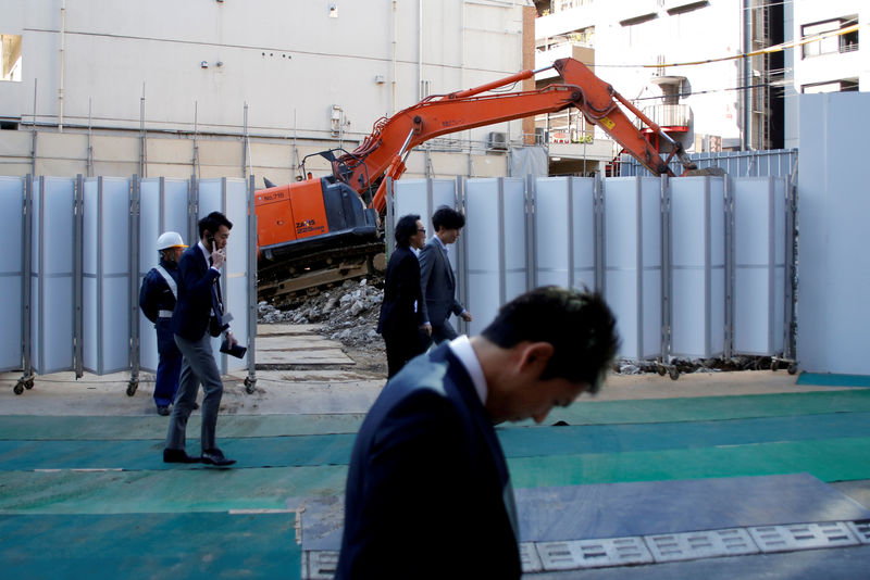 © Reuters. FILE PHOTO: Businessmen walk past heavy machinery at a construction site in Tokyo's business district