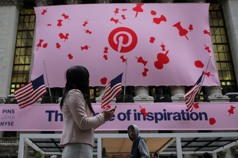 © Reuters. A woman uses her phone as a banner celebrating the IPO of Pinterest Inc. hangs on the front of the NYSE in New York