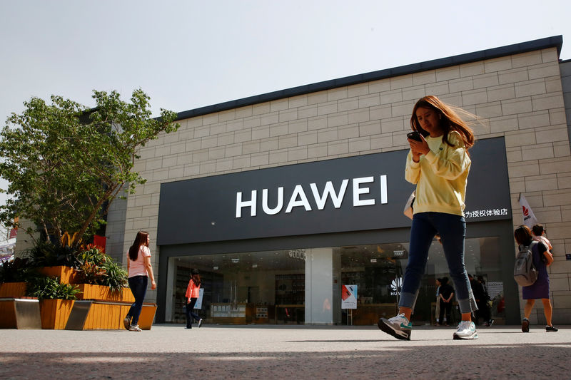 © Reuters. FILE PHOTO: A woman looks at her phone as she walks past a Huawei shop in Beijing