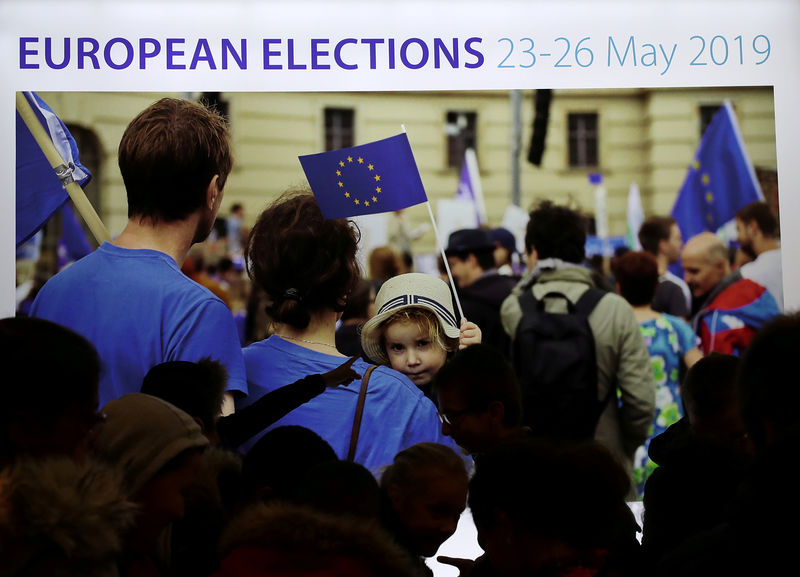 © Reuters. FILE PHOTO: People walk past a screen displaying an advertisement for the EU elections in Brussels