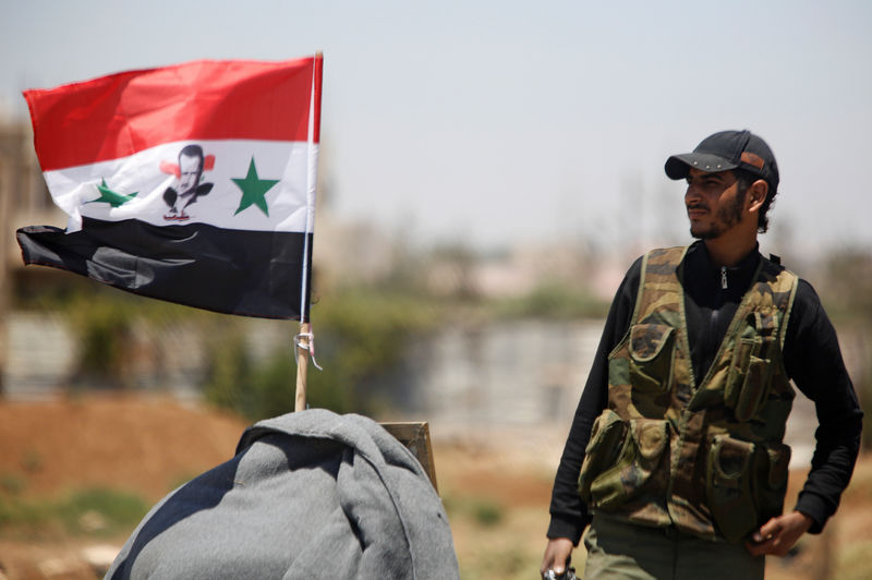 © Reuters. FILE PHOTO: A Syrian army soldier stands next to a Syrian flag in Umm al-Mayazen, in the countryside of Deraa