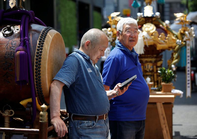 © Reuters. FILE PHOTO: A man uses his smartphone next to a Japanese traditional Taiko drum during the preprartion for the upcoming Kanda festival in Tokyo