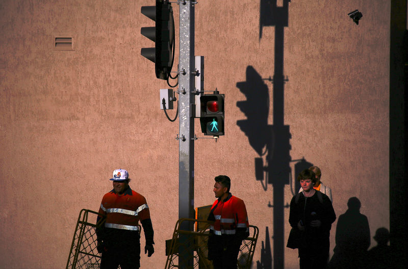 © Reuters. FILE PHOTO: Workers carry barriers as they wait to cross a street at a set of traffic lights with pedestrians at sunset in central Newcastle, located north of Sydney