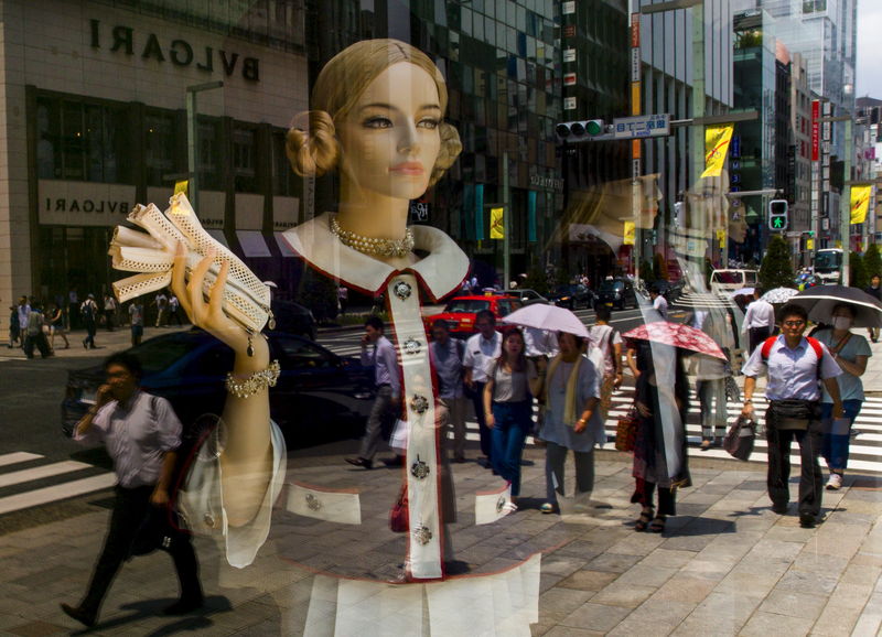 © Reuters. People are reflected in a shop window as they walk along a street in a shopping district in Tokyo