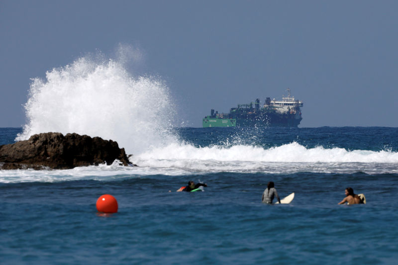 © Reuters. FILE PHOTO: People surf as a vessel involved in the construction of a natural gas pipeline is seen behind them in the Mediterranean Sea near Dor Beach