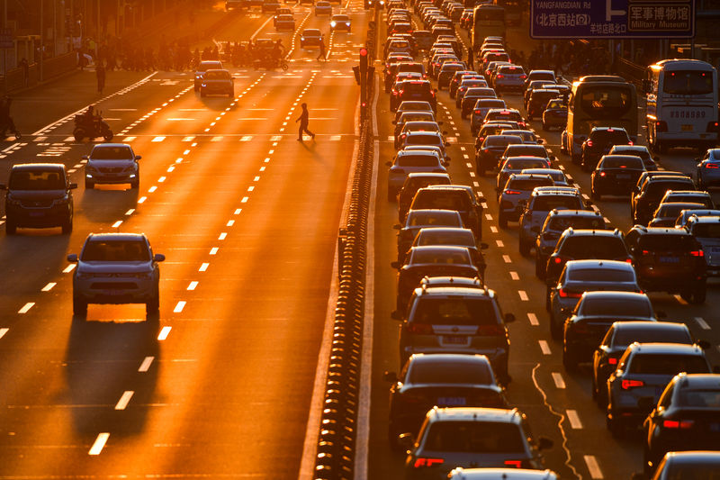 © Reuters. Pedestrian walks on a crossing next to cars in the traffic on a main road during sunset in Beijing