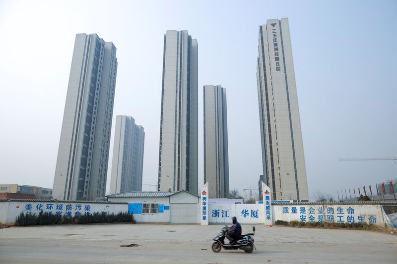 © Reuters. A man rides a scooter past apartment highrises that are under construction near the new stadium in Zhengzhou