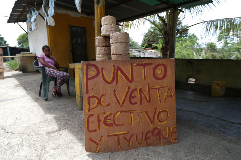 © Reuters. A woman sales 'Casabe', a kind of a flatbread made of yucca, next to a sign reading 'Sale point, cash and barter' near a road in Cupira