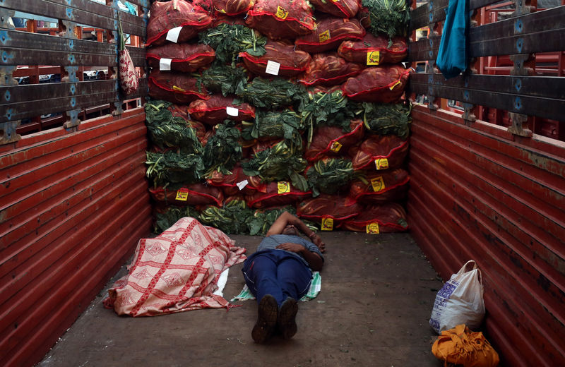 © Reuters. Men sleep in a supply truck loaded with sacks of cauliflower at a vegetable wholesale market in Mumbai