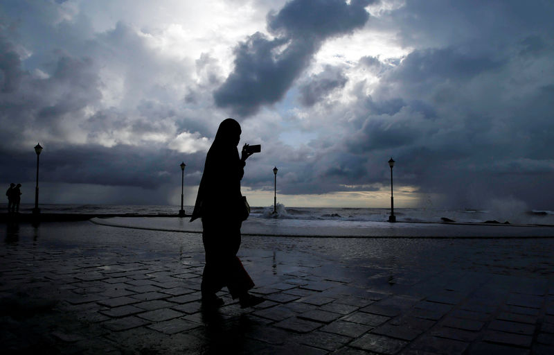 © Reuters. FILE PHOTO: A woman takes photographs with her mobile phone against the backdrop of monsoon clouds at a beach in Kochi