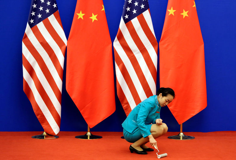 © Reuters. Una asistente limpia una alfombra junto a las banderas de China y Estados Unidos, antes de uan conferencia de prensa en el Gran Salón del Pueblo en Pekín
