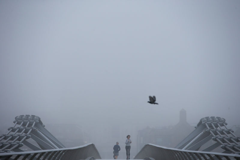 © Reuters. People walk across Millennium Bridge during heavy fog in London