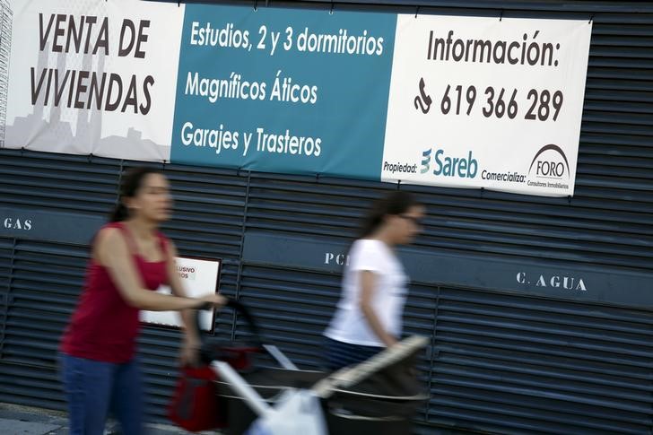 © Reuters. Varias personas pasan junto a un cartel de apartamentos en venta de la Sareb en Madrid