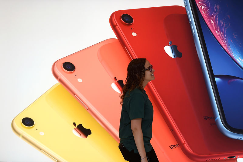 © Reuters. An Apple Store employee walks past an illustration of iPhones at the new Apple Carnegie Library during the grand opening and media preview in Washington