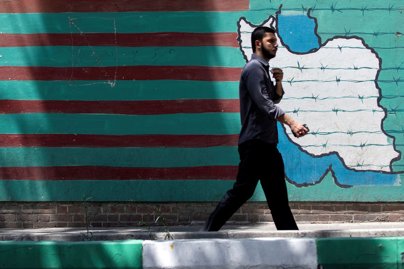 © Reuters. A man walks past the mural showing U.S. flag with barbed wire in Tehran