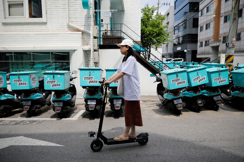 © Reuters. A woman on an electric scooter passes by Baemin Rider motorbikes in Seoul