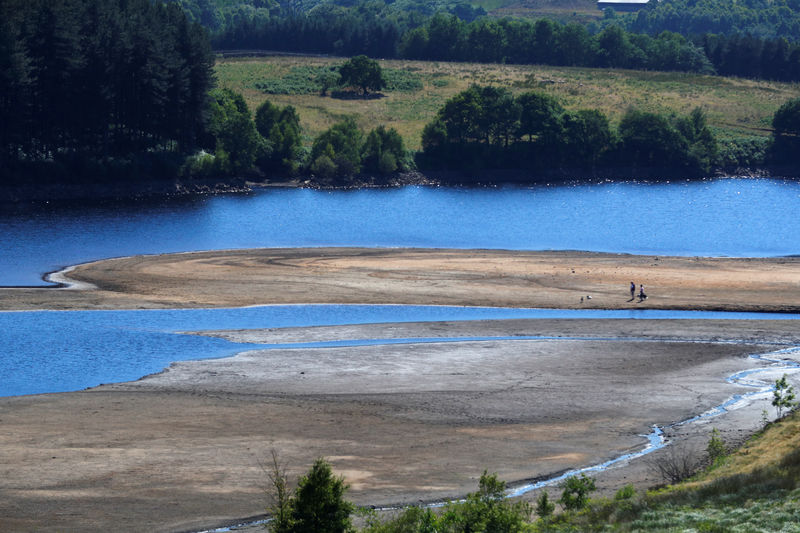 © Reuters. Two people take a walk by the water's edge, where the water level has dropped significantly during the U.K. heatwave, of Torside Reservoir in Longdendale
