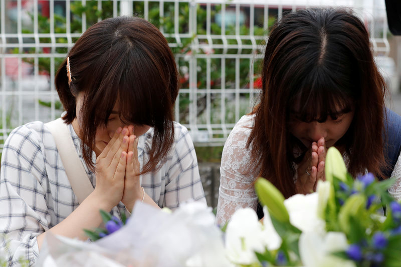 © Reuters. Women pray in front of a row bouquets placed out for victims of the torched Kyoto Animation building in Kyoto
