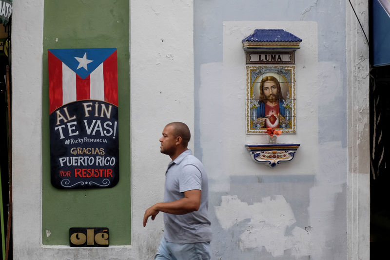 © Reuters. FILE PHOTO: A man walks past a sign that reads "You are finally leaving. Ricky resign. Thanks Puerto Rico for resisting" in Old San Juan