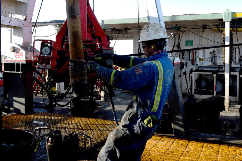 © Reuters. A worker wrestles a stand of drill pipe into place on a drilling rig near Midland