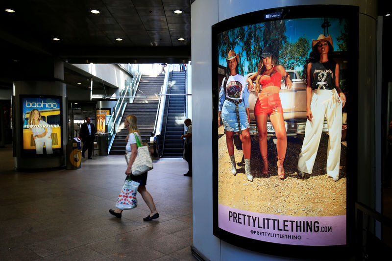 © Reuters. FILE PHOTO: A shopper walks pass advertising billboards for Boohoo and for 'Pretty Little Things', a Boohoo brand, at Canary Wharf DLR station in central London