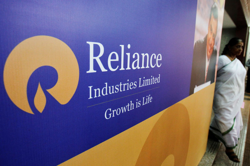 © Reuters. FILE PHOTO: A woman walks past a poster of Reliance Industries installed outside the venue of the company's annual general meeting in Mumbai