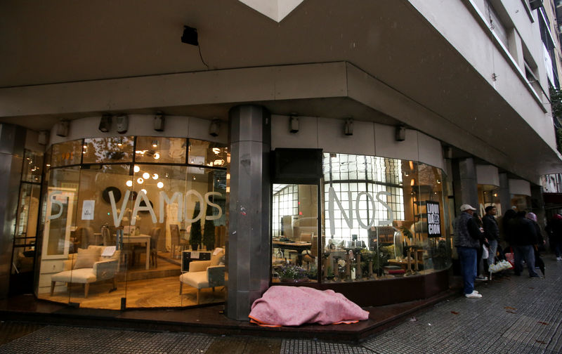 © Reuters. FILE PHOTO: A homeless person sleeps outside a shop with a graffiti on its windows that reads "we are leaving", one day after a national blackout, in Buenos Aires