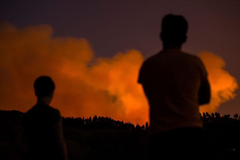 © Reuters. Two people look at flames and smoke from a forest fire, seen in the village of Valleseco