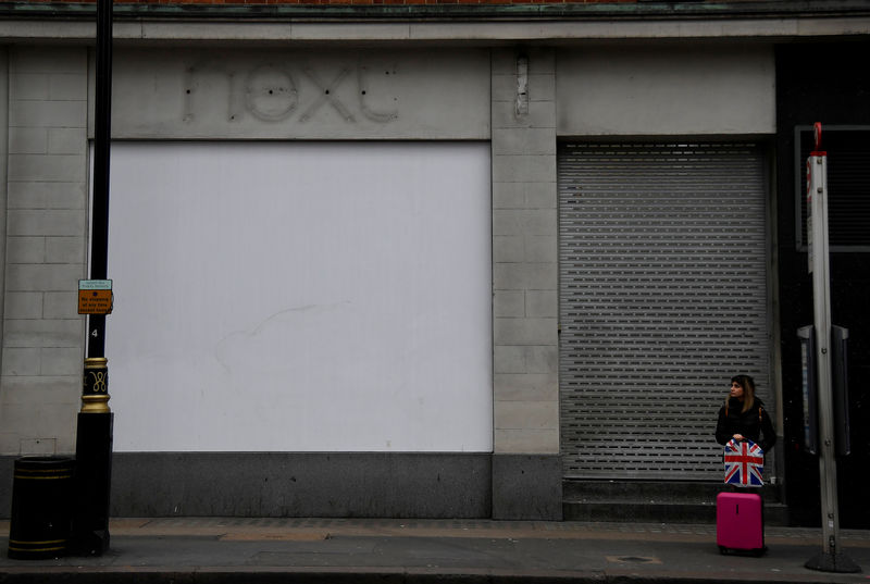 © Reuters. FILE PHOTO: A shopper waits at a bus stop beside signage for a former branch of the British clothing retailer Next, off Oxford Street in London, Britain