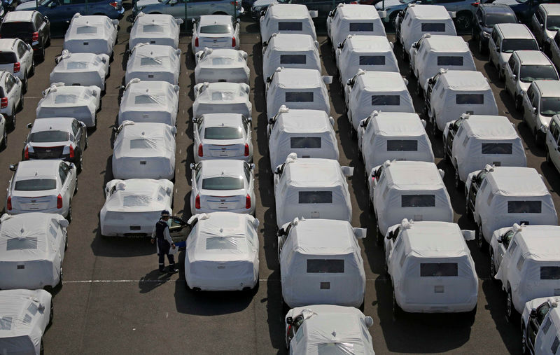 © Reuters. A man works among imported cars covered with a white cloth in a port in Yokohama