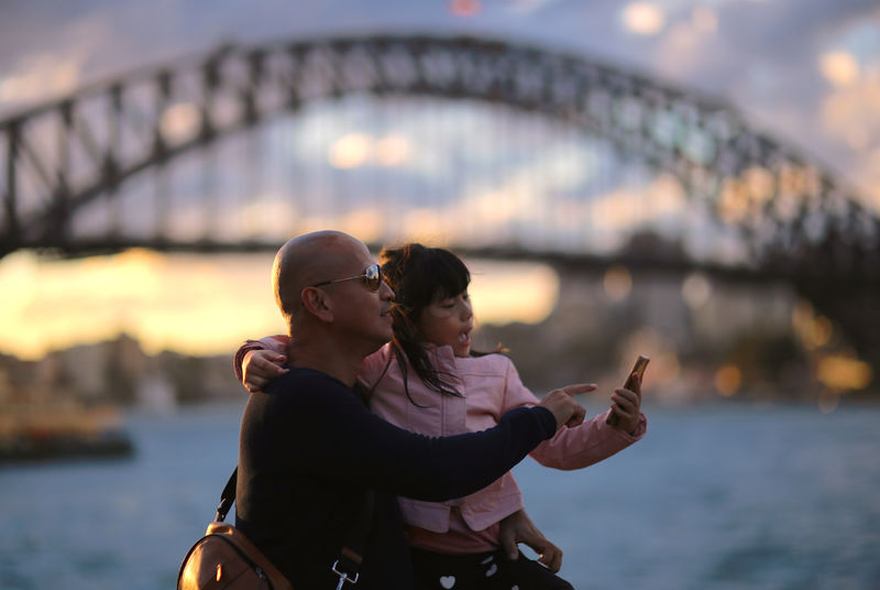 © Reuters. FILE PHOTO: Tourists look at a phone as they stand in front of the Sydney Harbour Bridge at sunset in Australia