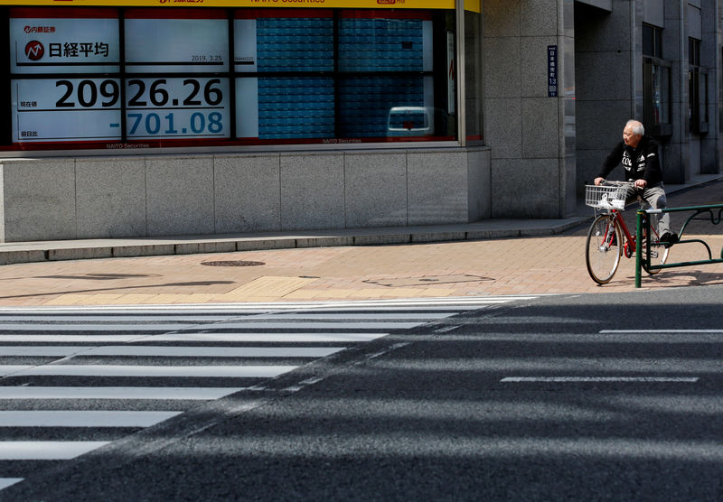 © Reuters. FILE PHOTO: A man in a bicycle stops in front of an electronic board showing the Nikkei stock index outside a brokerage in Tokyo