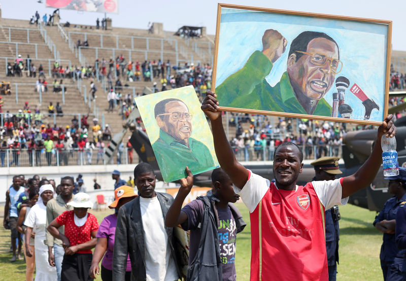© Reuters. Mourners hold paintings with the face of former Zimbabwean president Robert Mugabe, as they queue to pay their last respects as he lies in state at the at Rufaro stadium, in Mbare