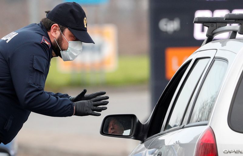 © Reuters. FILE PHOTO: A policeman wearing a face mask warns a driver on the road between Codogno and Casalpusterlengo, which has been closed by the Italian government due to a coronavirus outbreak in northern Italy