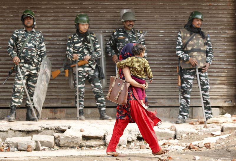 © Reuters. A woman carrying a child walks past security forces in a riot affected area after clashes erupted between people demonstrating for and against a new citizenship law in New Delhi