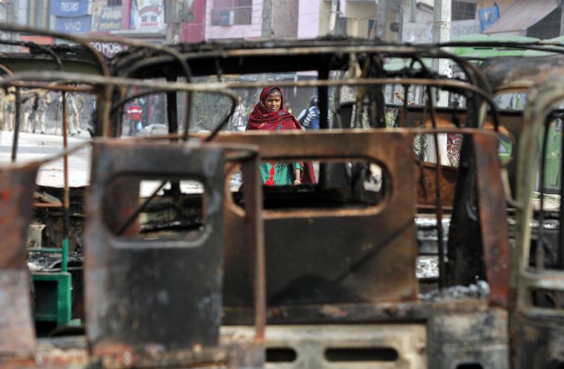 © Reuters. A woman walks past charred vehicles in a riot affected area following clashes between people demonstrating for and against a new citizenship law in New Delhi