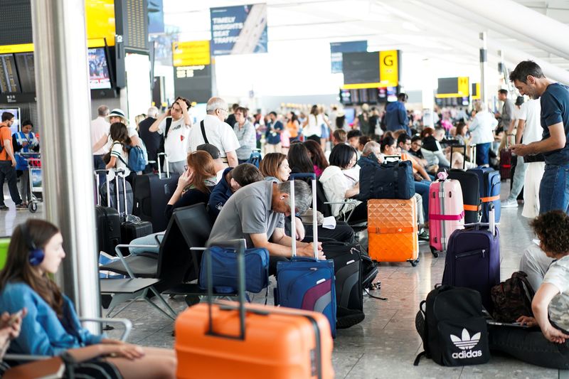 © Reuters. FILE PHOTO: People wait inside Terminal 5 at Heathrow Airport as IT problems caused delays in London