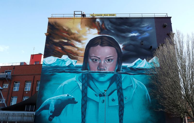 © Reuters. Men tie a banner to a building where a mural of Greta Thunberg has been painted, in Bristol