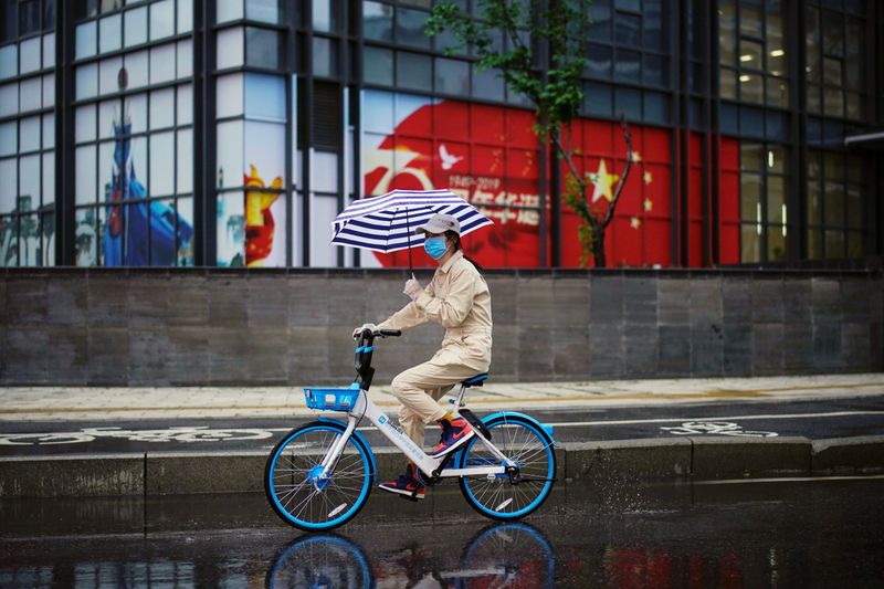 © Reuters. Woman rides a shared bicycle past an image of the Chinese flag in Wuhan
