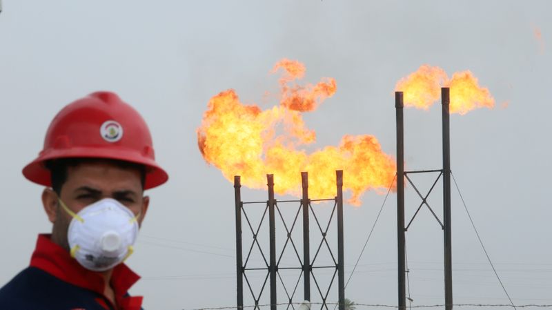 © Reuters. FILE PHOTO: An oil worker in a protective mask, with flare stacks at Iraq's Nahr Bin Umar oilfield in the background protective mask, following an outbreak of coronavirus, north of Basra