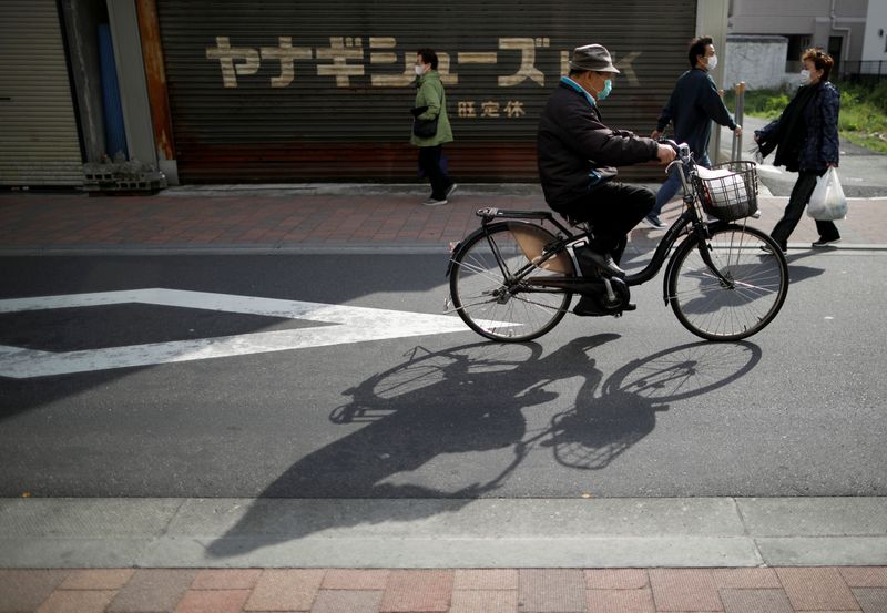 © Reuters. People wearing protective face masks walk on the street after the government announced state of emergency at Sugamo district in Tokyo, Japan