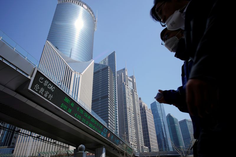 &copy; Reuters. Pedestrians wearing face masks walk near an overpass with an electronic board showing stock information in Shanghai