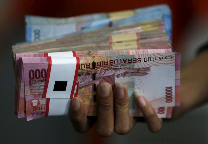 &copy; Reuters. FILE PHOTO:  An employee of a money changer holds a stack of Indonesia rupiah notes before giving it to a customer in Jakarta