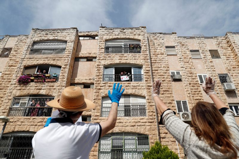 &copy; Reuters. Harry and Janny Brodesky, son-in-law and daughter of Elias Feinzilberg, a 102-year-old Holocaust survivor, wave as they stand by his home in Jerusalem as Israel marks Holocaust Remembrance Day under coronavirus disease (COVID-19) restrictions