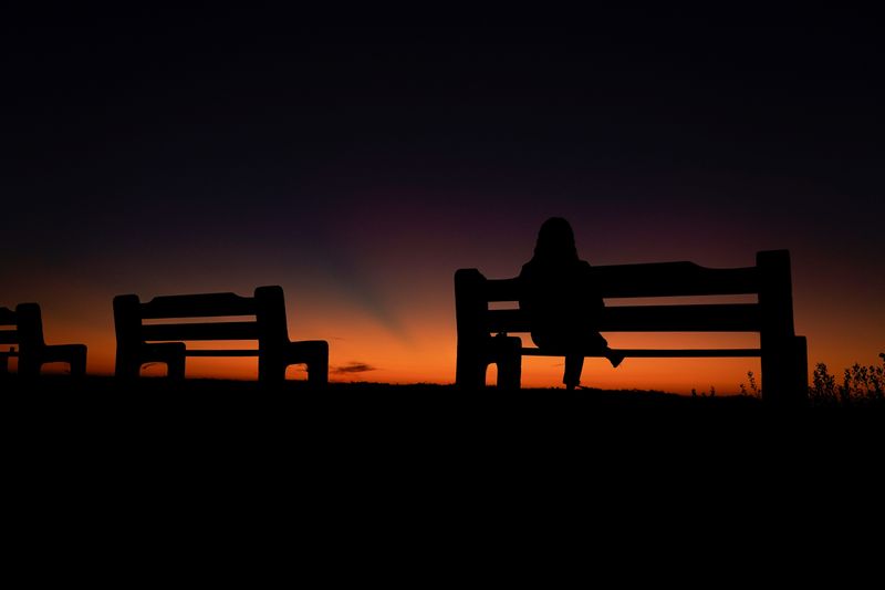 &copy; Reuters. A women sits alone on a park bench watching the sky after sun set in Encinitas, California