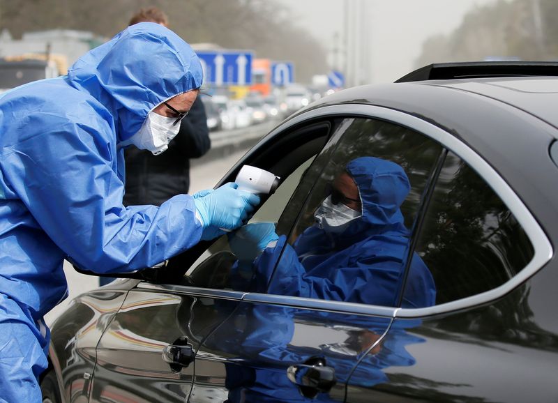 &copy; Reuters. Медработник измеряет температуру водителю и пассажирам автомобиля на КПП на окраине Киева